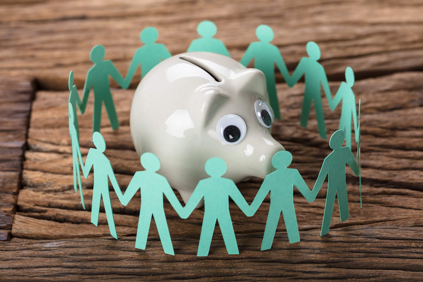 humans holding hands around a piggy bank